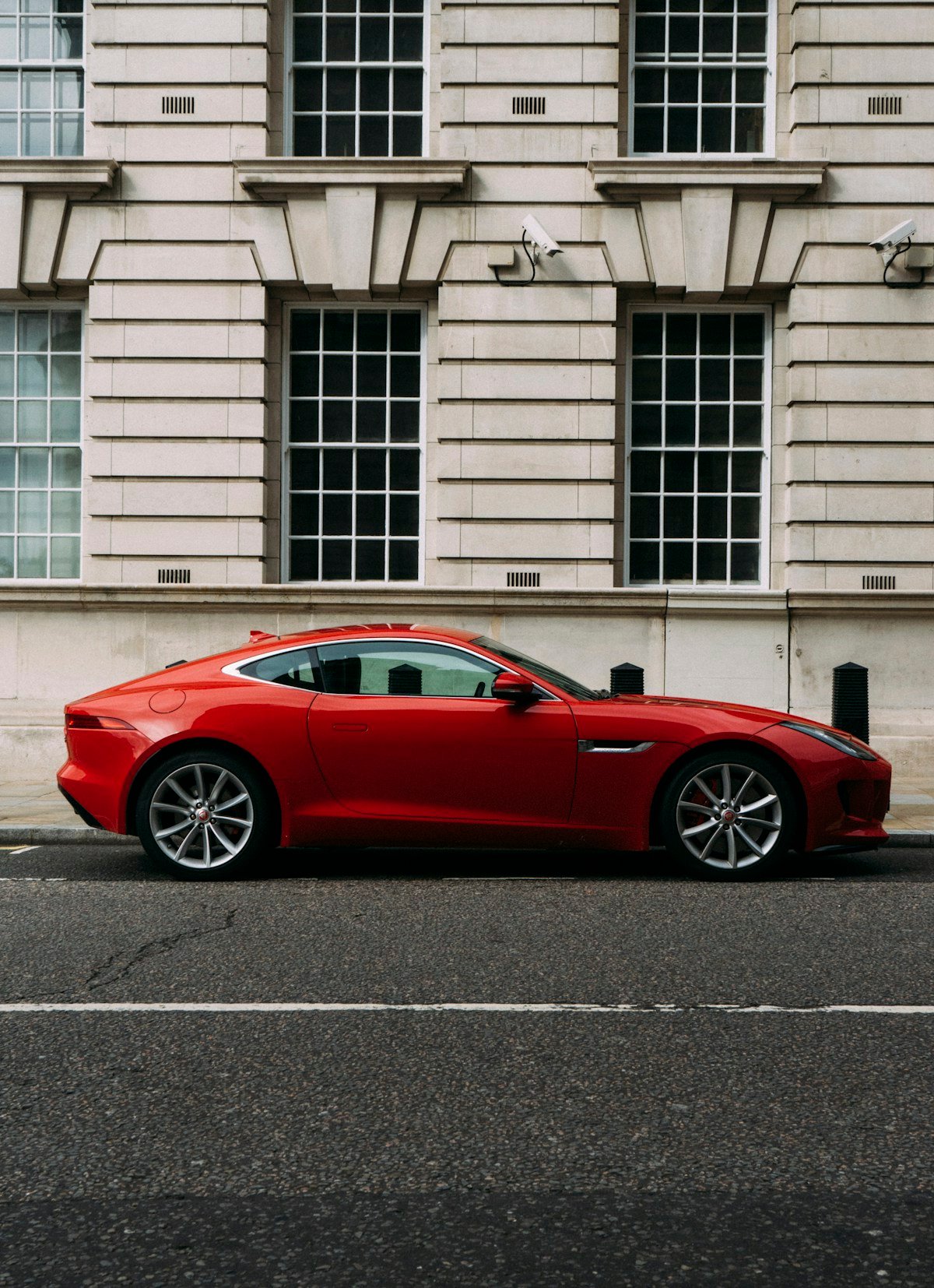 Jaguar rouge devant une façade en pierre, photographie d’ambiance